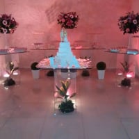 Mesa de bolo e doces em vidro transparente com iluminação e paisagismo interno.